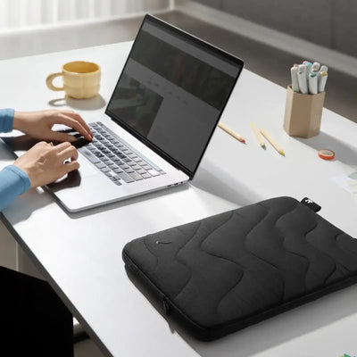 Minimalistyczne biurko z laptopem, czarnym etui na laptop, kubkiem i przyborami biurowymi do home office