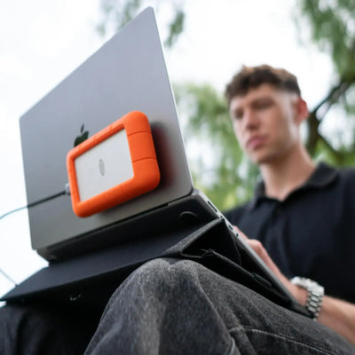 Mężczyzna pracujący na laptopie z zewnętrznym dyskiem SSD w pomarańczowej obudowie, praca mobilna