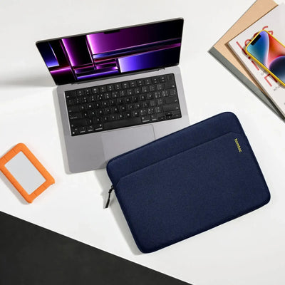 Laptop na biurku, niebieskie etui ochronne na laptopa, dysk zewnętrzny, smartfon i czasopisma. Idealny zestaw do pracy zdalnej i home office.