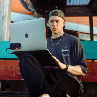 Mężczyzna z laptopem Apple i podłączonym dyskiem SSD siedzi na zewnątrz na ławce